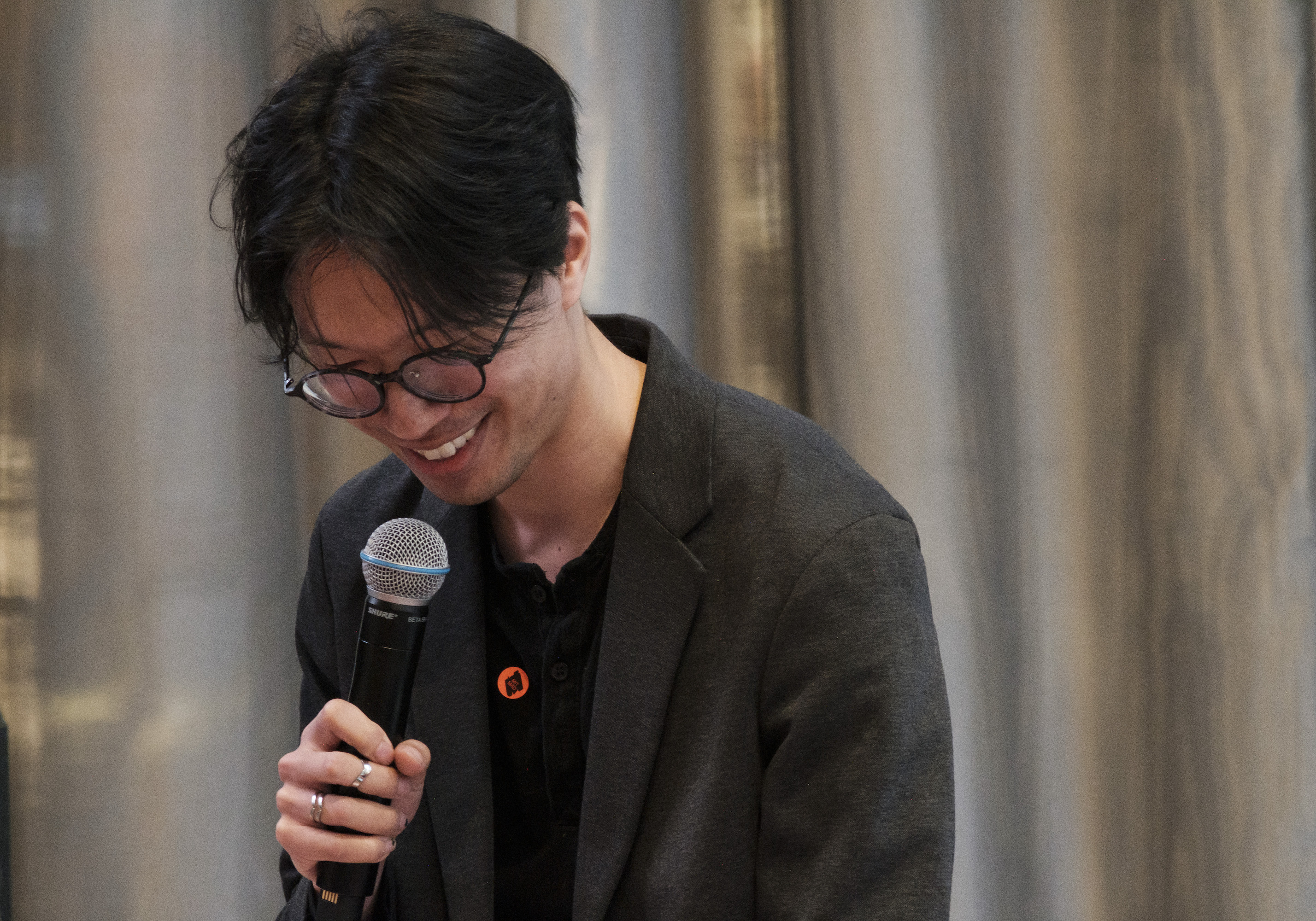 A professional photo of Jonathan Zong. He is looking down and smiling while holding a microphone.